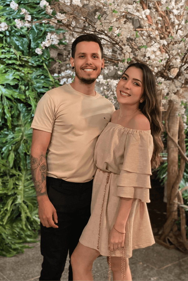 Casal sorridente posando em frente a árvores com flores brancas